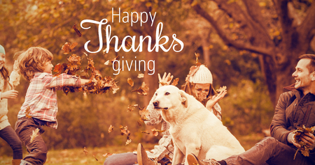 Thanksgiving greeting text against young family with a dog in leavesの写真素材