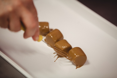 Worker putting chocolate coated marshmallows on tray in kitchenの写真素材