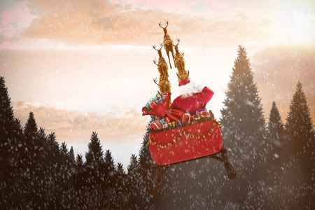 Rear view of Santa Claus riding on sled against snow falling on fir tree forestの写真素材