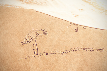 Umbrella and sun drawn on sand at beachの写真素材