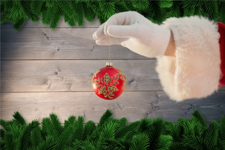 Santa claus holding christmas bauble against digitally generated backgroundの写真素材