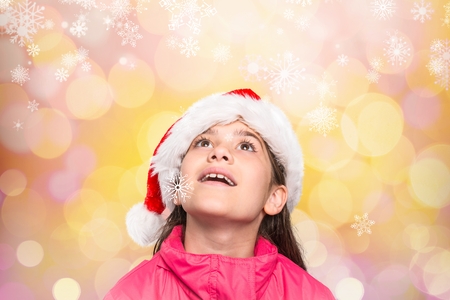 Cute girl in santa hat pretending to be amazed by digitally generated colorful backgroundの写真素材