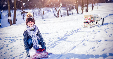 Portrait of cute boy picking up present against snow fallingの写真素材