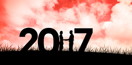 Silhouettes shaking hands against red sky over grass