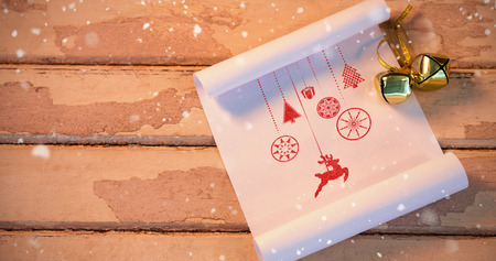 Snow falling against bells and paper on wooden plank