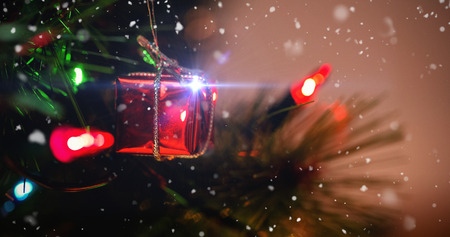 Snow falling against fairy light and small gift box hanging on christmas treeの写真素材