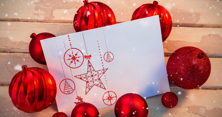 Snow falling against christmas bauble ball and paper on wooden plankの写真素材