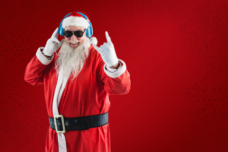 Cheerful Santa Claus showing hand sign while listening to music on headphones against red snowflake backgroundの写真素材