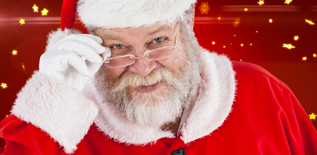 Santa Claus holding spectacles against bright star pattern on redの写真素材
