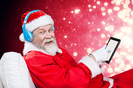 Portrait of Santa Claus listening music with digital tablet  against light design shimmering on redの写真素材