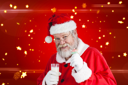 Cheerful Santa Claus showing glass of milk and star shape cookie against bright star pattern on redの写真素材
