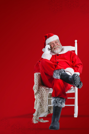 Santa claus talking on mobile phone against red snowflake backgroundの写真素材