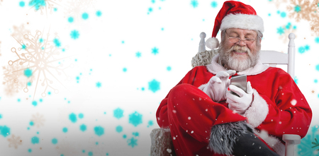 Happy Santa Claus messaging with mobile phone against snowflake patternの写真素材