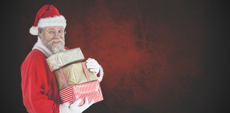 Portrait of Santa Claus holding Christmas gifts against dark backgroundの写真素材