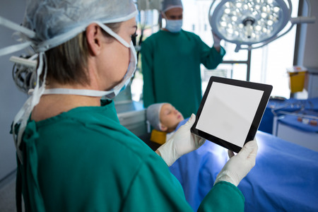 Surgeon using digital tablet while operating patient in operation theaterの写真素材