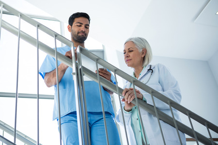 Doctors discussing over digital tablet while standing on stairs in hospitalの写真素材
