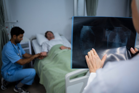 Doctor analyzing x-ray in ward while surgeon consulting patient in background