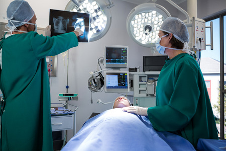 Surgeons discussing x-ray while operating patient in operation theaterの写真素材