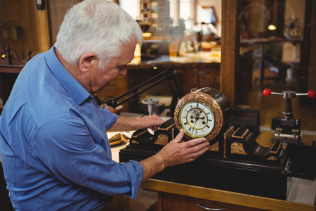 Attentive horologist checking a clock in workshopの写真素材