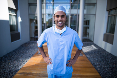 Portrait of male surgeon standing with hands on hip in hospital corridorの写真素材