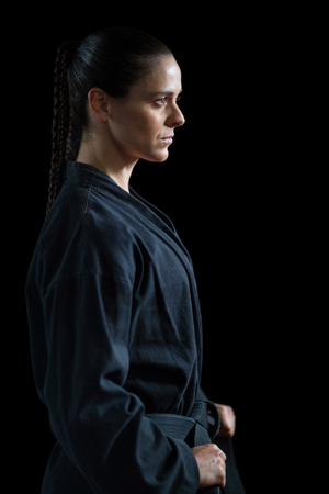 Confident karate player holding her belt against black backgroundの写真素材