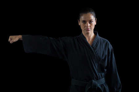 Female karate player performing karate stance against black backgroundの写真素材