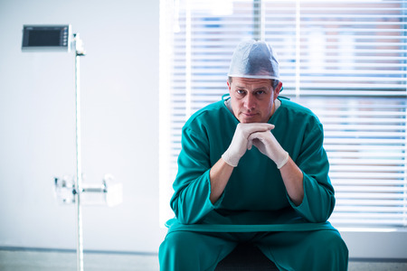 Portrait of male surgeon sitting in corridor of hospitalの写真素材
