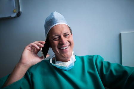 Smiling surgeon talking on mobile phone in hospitalの写真素材