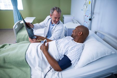 Doctor discussing x-ray with patient in ward of hospitalの写真素材