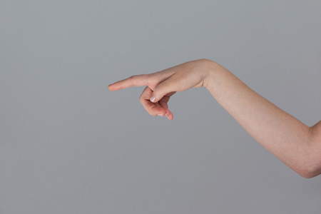 Hand of a woman pointing sideways against grey background