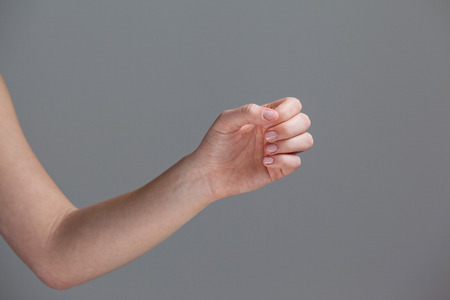 Hand of a woman with manicured nails against grey background