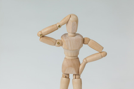 Confused wooden figurine standing with hand on head against white backgroundの写真素材