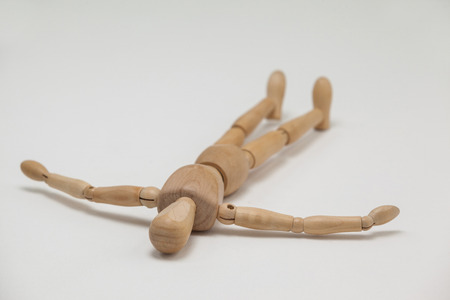Wooden figurine lying on floor with arms spread against white backgroundの写真素材