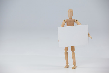 Wooden figurine standing and holding a white placard against white backgroundの写真素材