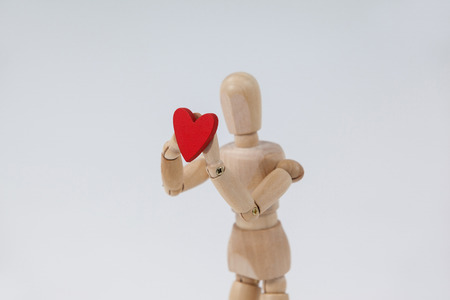 Wooden figurine standing and holding a red heart against white backgroundの写真素材