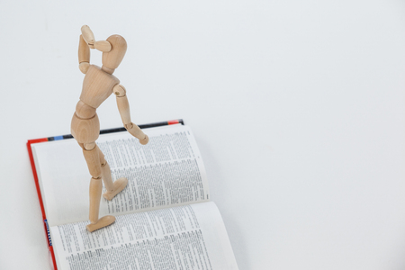 Wooden figurine standing on an open book against white backgroundの写真素材
