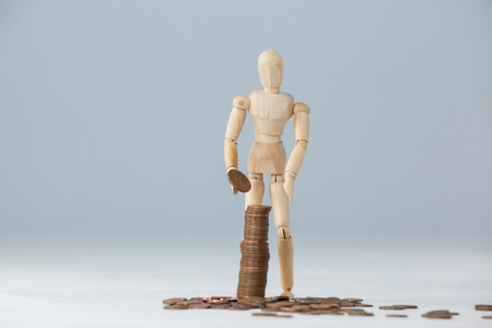 Wooden figurine standing and making stack of coins against white background