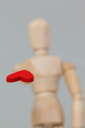 Wooden figurine standing and giving a red heart against white backgroundの写真素材