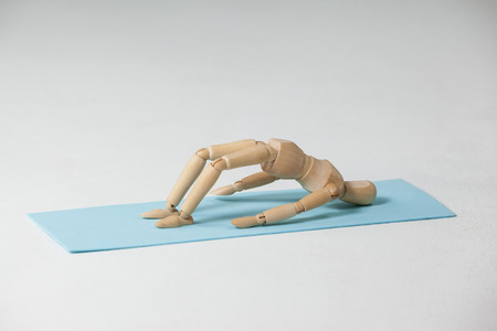 Wooden figurine exercising on exercise mat against white backgroundの写真素材