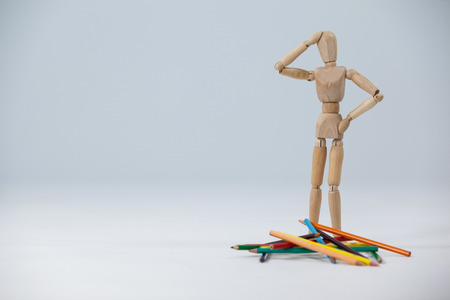 Confused wooden figurine standing near a heap of color pencils against white backgroundの写真素材