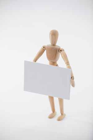 Wooden figurine standing and holding a white placard against white backgroundの写真素材