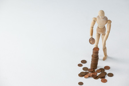 Wooden figurine standing and making stack of coins against white backgroundの写真素材