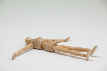 Wooden figurine lying on floor with arms spread against white backgroundの写真素材
