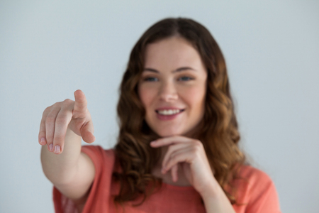Portrait of a woman pretending to touch an invisible screen against grey backgroundの写真素材