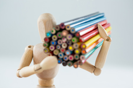 Wooden figurine carrying bunch of pencils against white backgroundの写真素材