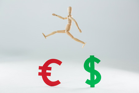 Wooden figurine jumping over dollar and euro symbol against white backgroundの写真素材