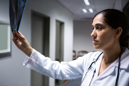 Female doctor examining x-ray report in corridor at hospitalの写真素材