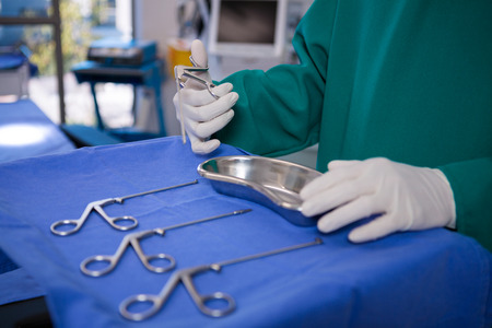 Mid section of surgeon holding surgical tool in operation theater of hospital