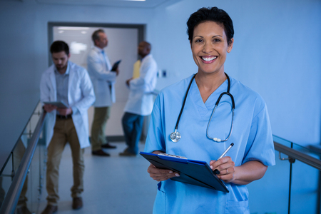 Portrait of female nurse writing in clipboard in corridor at hospitalの写真素材
