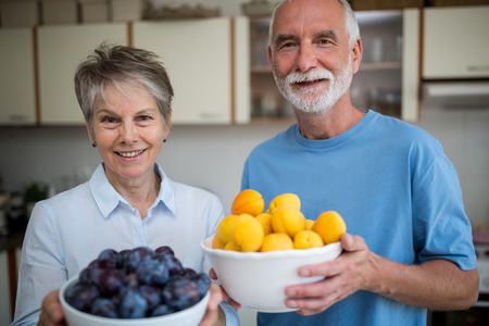 Portrait of senior couple holding bowl of apricot and grapes in kitchen